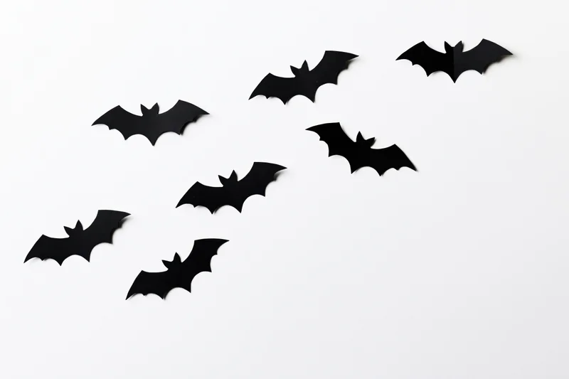 Seven black paper bat cutouts arranged diagonally on white background