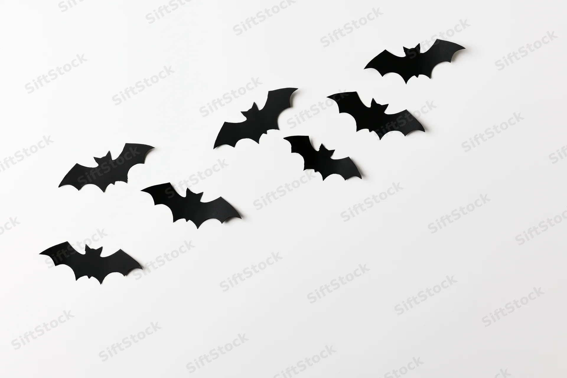 Seven black paper bat cutouts arranged diagonally on white surface