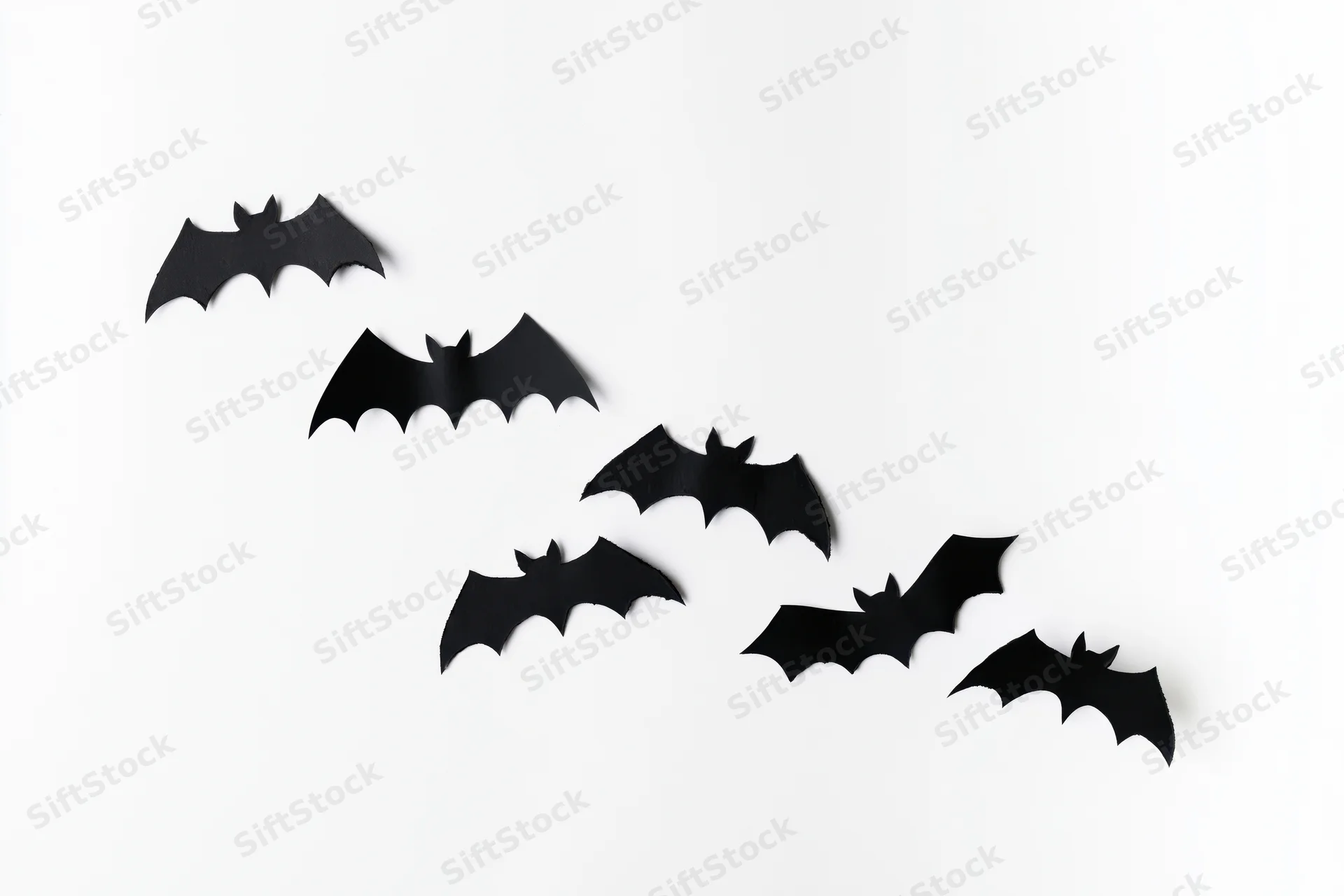 Black paper bat cutouts arranged diagonally on white background