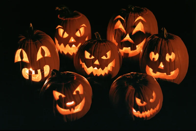 Seven carved jack-o-lanterns glowing in the dark with different spooky faces