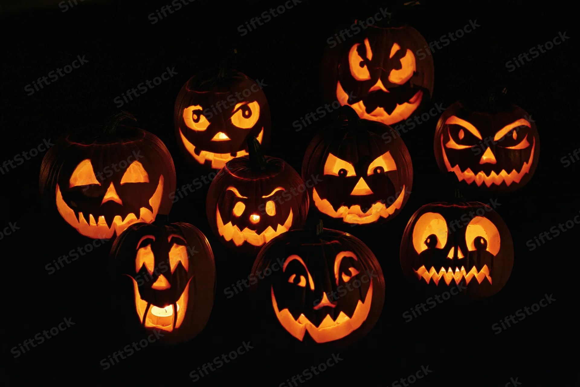 Seven carved jack-o-lanterns glowing with different expressions in the dark