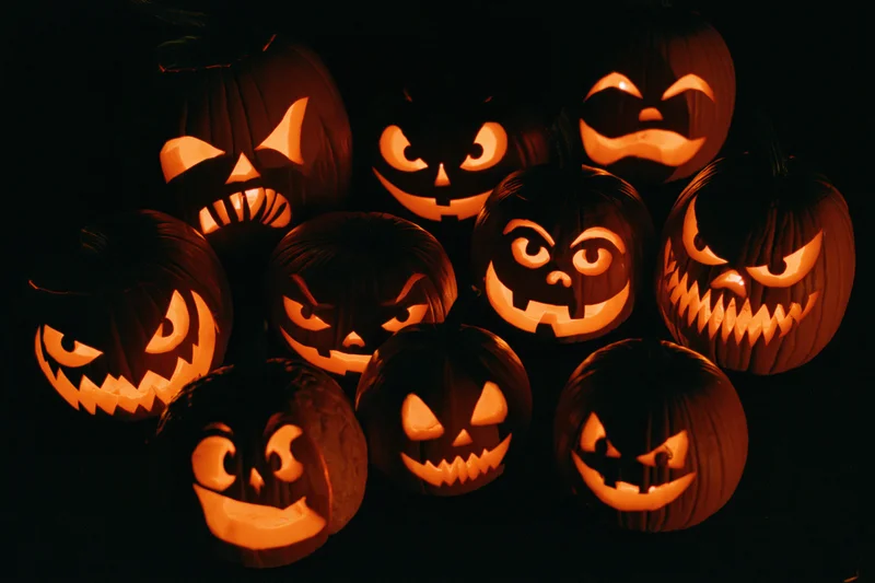 Glowing carved pumpkins with varied spooky faces arranged in a group at night