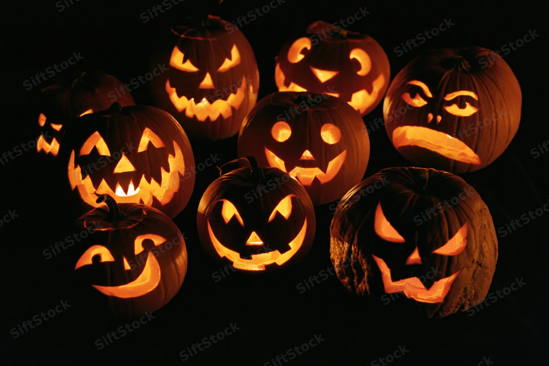 Seven carved jack-o-lanterns glowing with different facial expressions in the dark