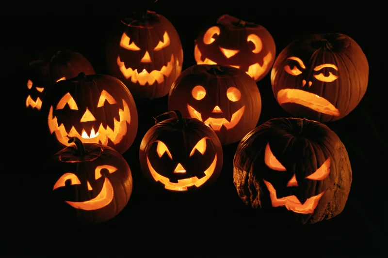 Seven carved jack-o-lanterns glowing with different facial expressions in the dark