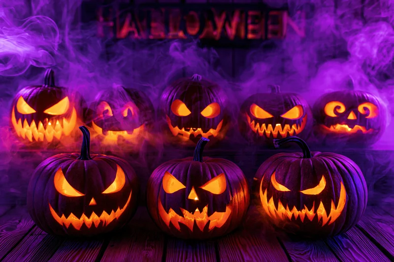 Seven carved jack-o-lanterns glowing with orange light on a wooden table in purple smoke