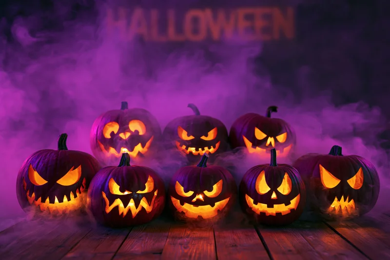 Seven carved jack-o-lanterns glowing with orange light on a wooden floor in purple smoke