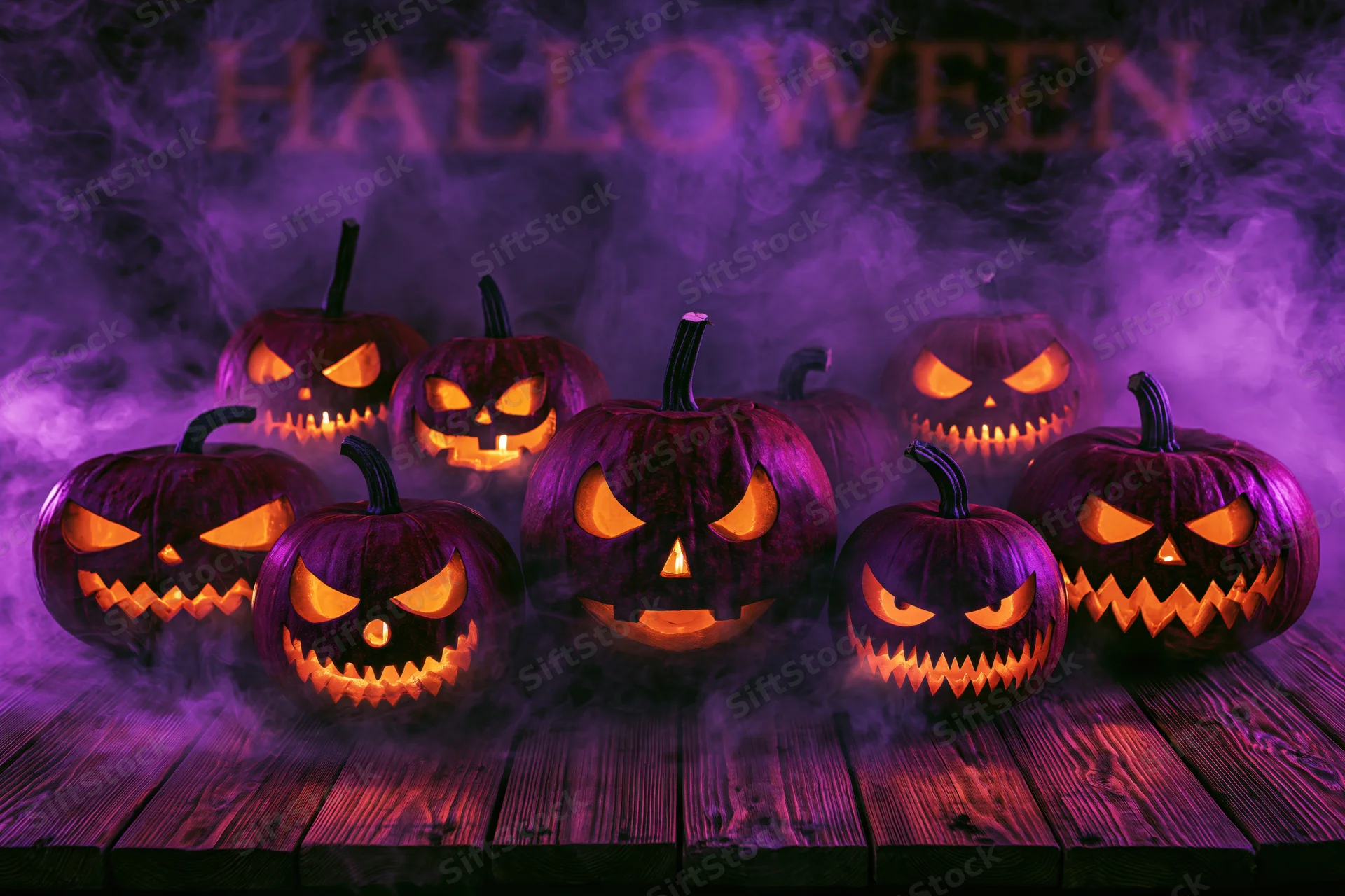 Seven carved jack-o-lanterns glowing with orange light on a wooden table in purple smoke