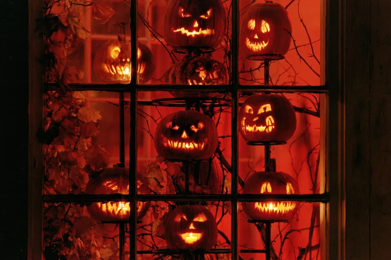 Glowing jack-o-lanterns arranged on a tiered metal stand behind a window pane