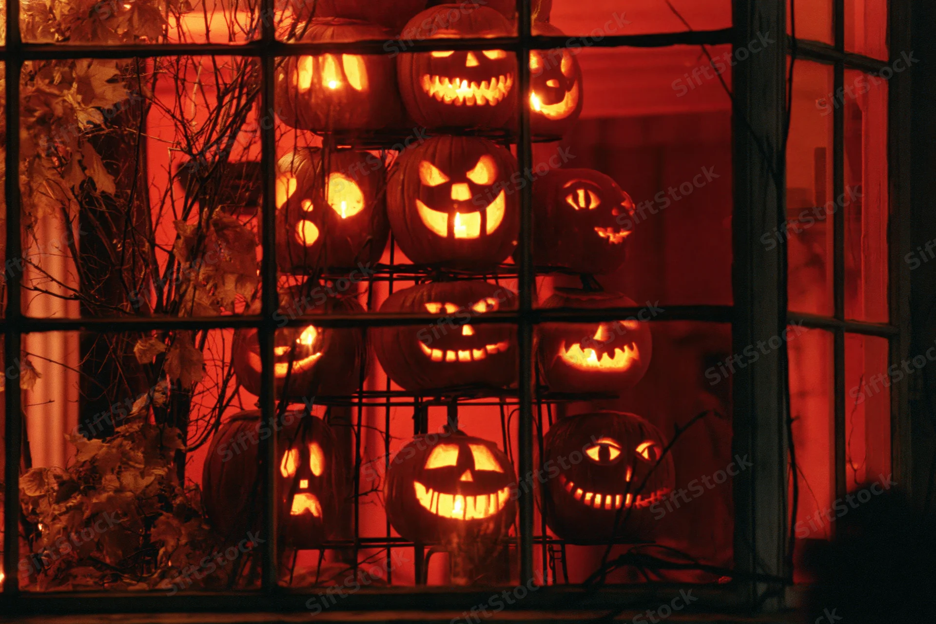 Glowing jack-o-lanterns stacked on a metal tiered stand viewed through a window at night