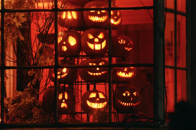 Glowing jack-o-lanterns stacked on a metal tiered stand viewed through a window at night