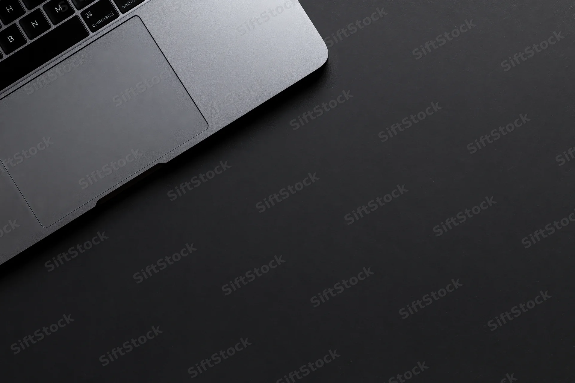 Silver aluminum laptop partially visible on black surface with copyspace