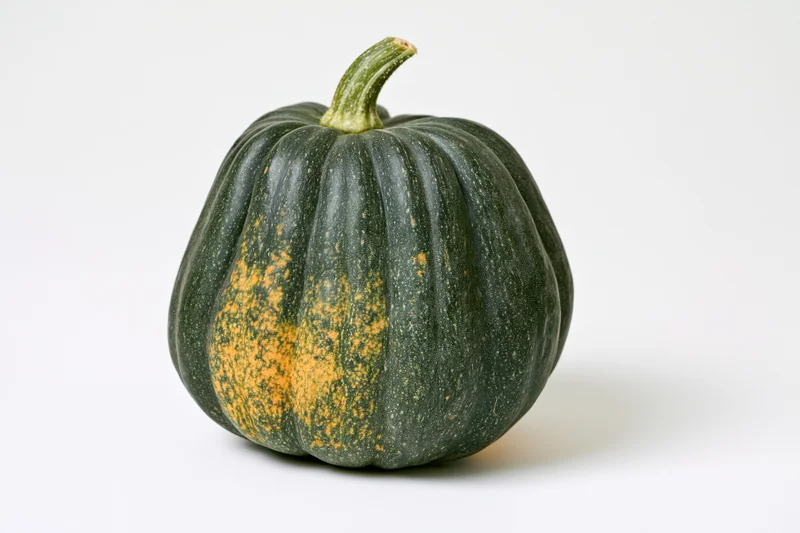 Acorn squash resting on a white surface with visible ribs and green-orange skin