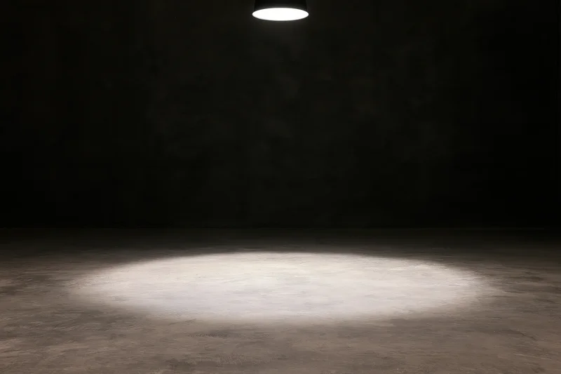 Single overhead spotlight casting a narrow beam of white light on a concrete floor in a dark room