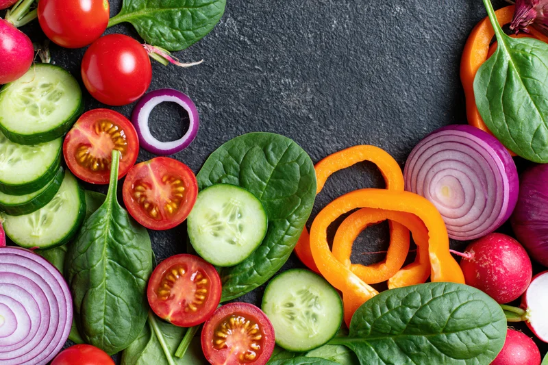 Fresh sliced vegetables arranged in a flat lay border on dark slate surface