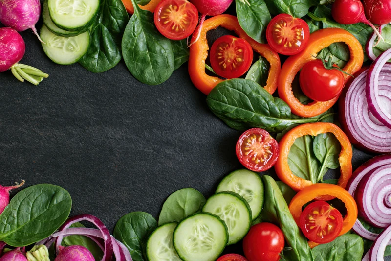Fresh vegetables arranged in a border on dark surface with copyspace