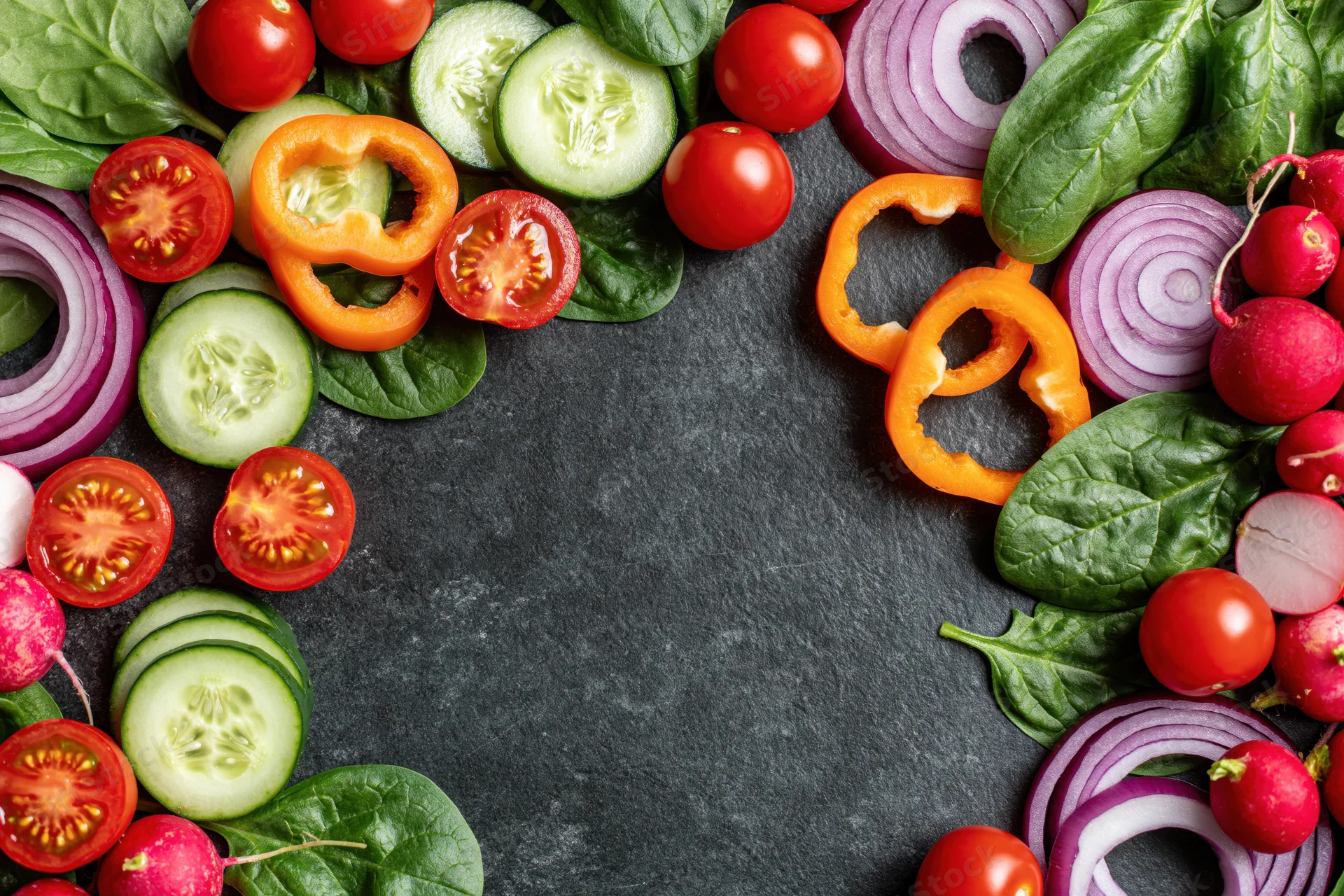 Fresh vegetables arranged in a border around a dark slate surface with copyspace in center