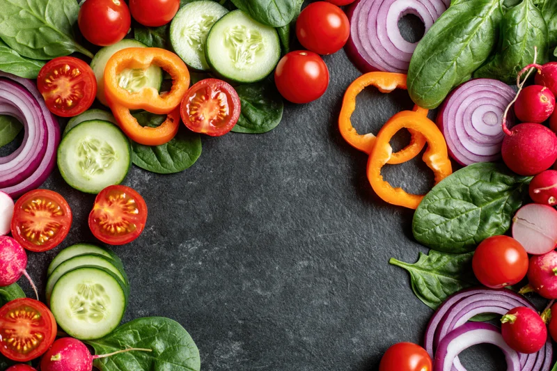 Fresh vegetables arranged in a border around a dark slate surface with copyspace in center