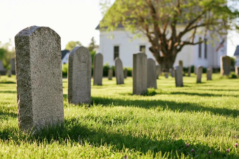 Rows of granite gravestones in a grassy churchyard with a white church in the background