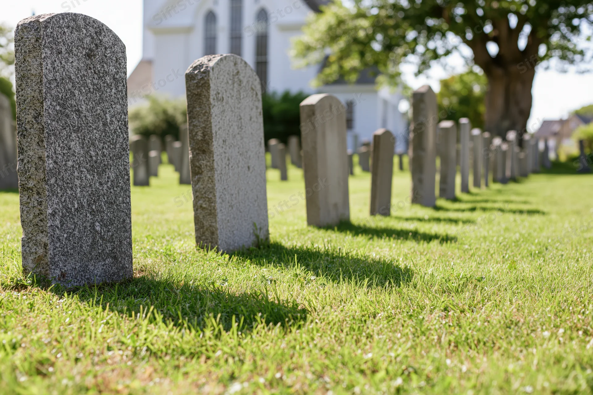 Rows of granite gravestones in a grassy churchyard with a white church in the background