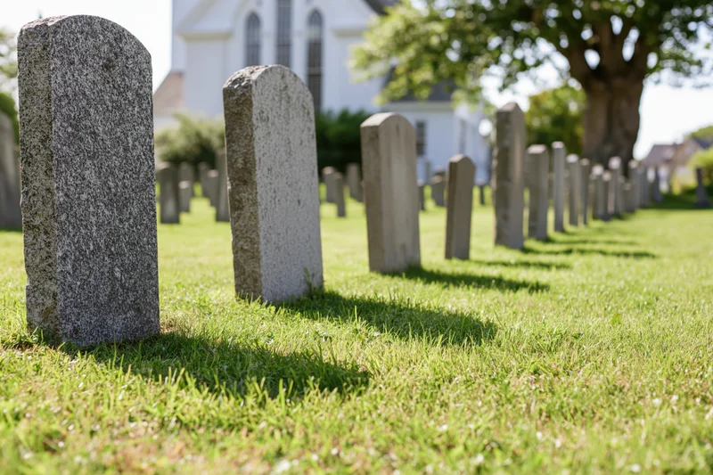 Rows of granite gravestones in a grassy churchyard with a white church in the background
