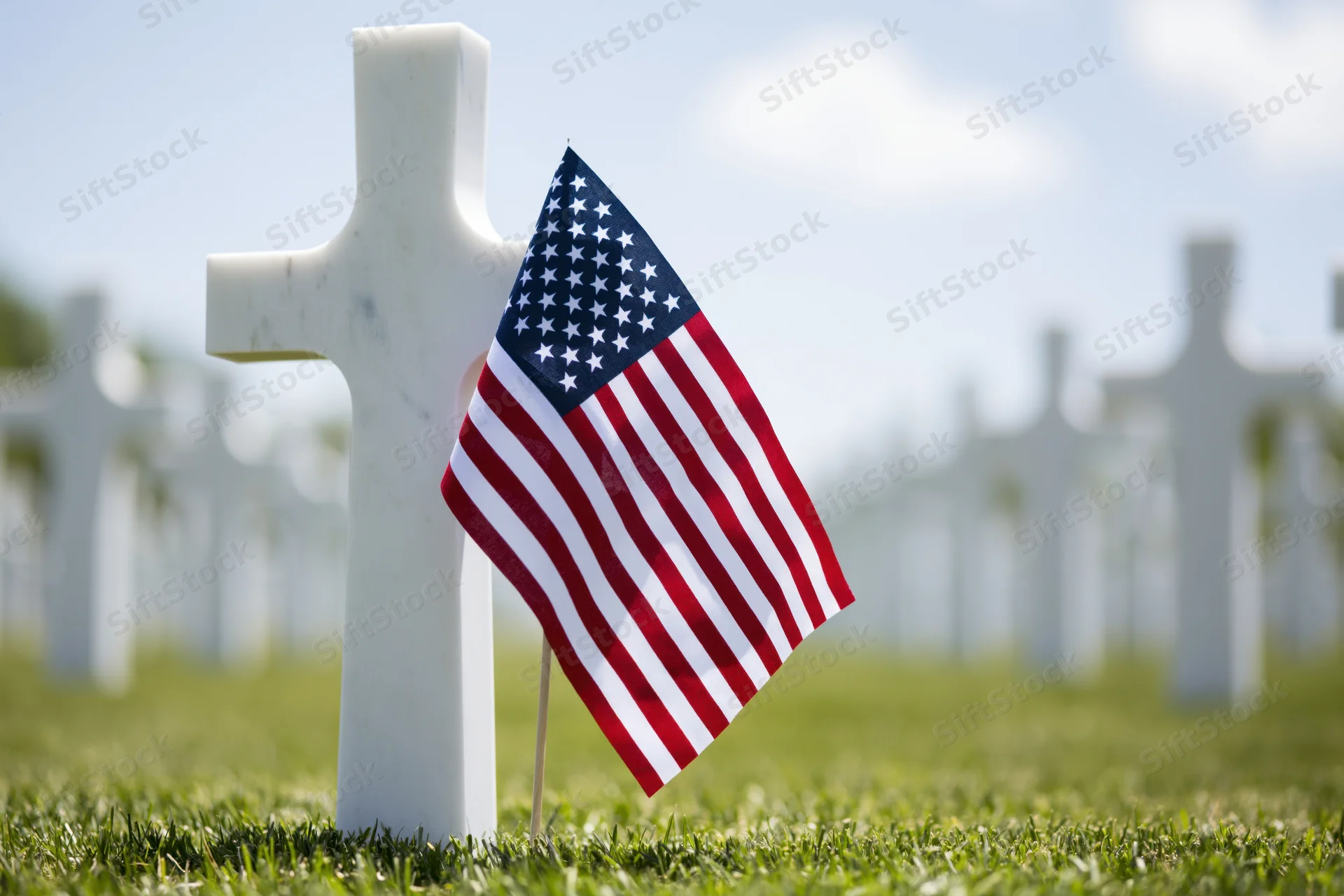Small american flag planted at base of white marble cross in cemetery