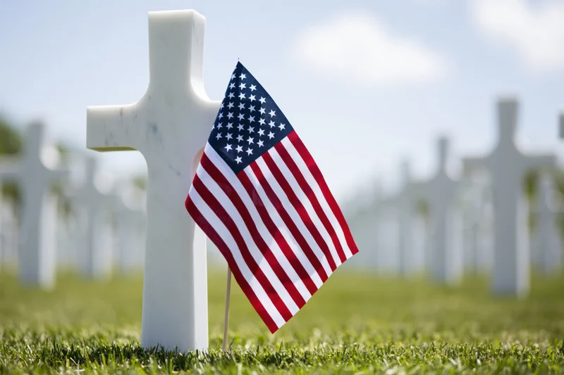 Small american flag planted at base of white marble cross in cemetery