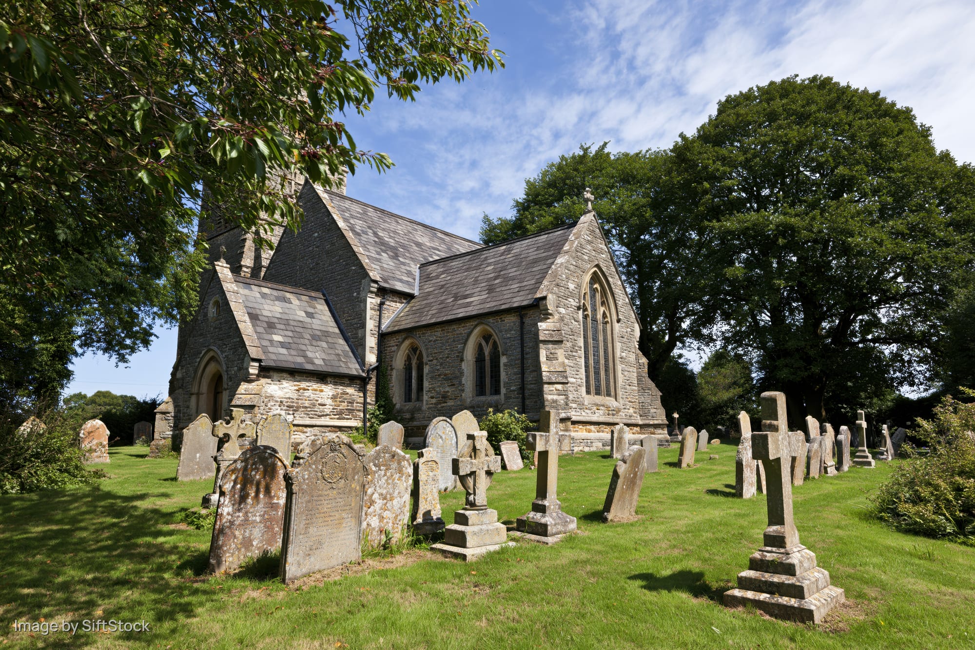 Stone victorian parish church with graveyard and tombstones in rural countryside under blue sky