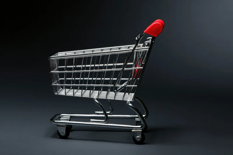 Small empty metal shopping cart with red plastic handle on dark studio background