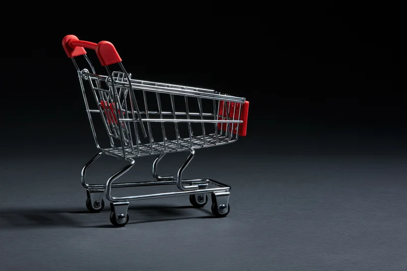 Small empty metal shopping cart with red plastic handles on dark surface