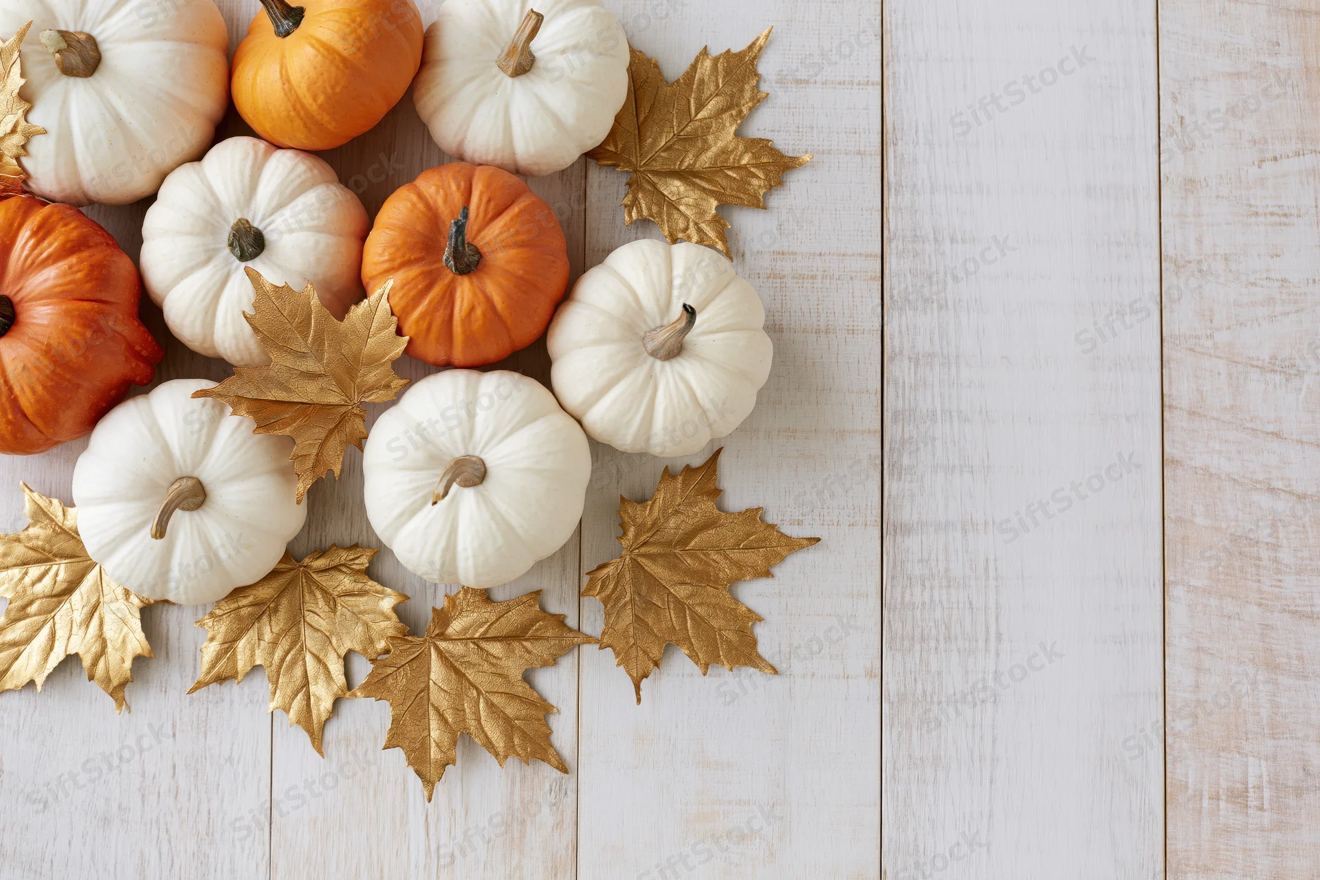 Small white and orange pumpkins with gold leaves arranged on a white wooden table