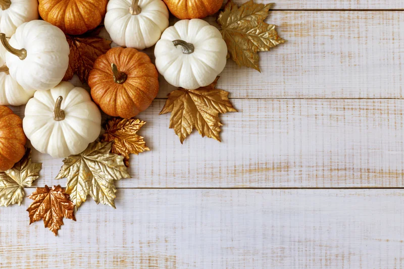 Small white and orange decorative pumpkins with gold leaves arranged on a white wooden table