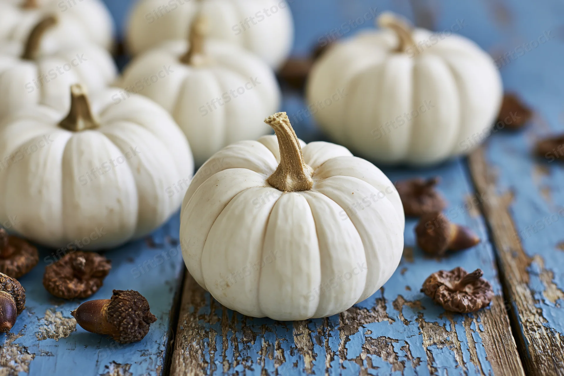 Small white ghost pumpkins arranged on a weathered blue painted wooden table with scattered acorns