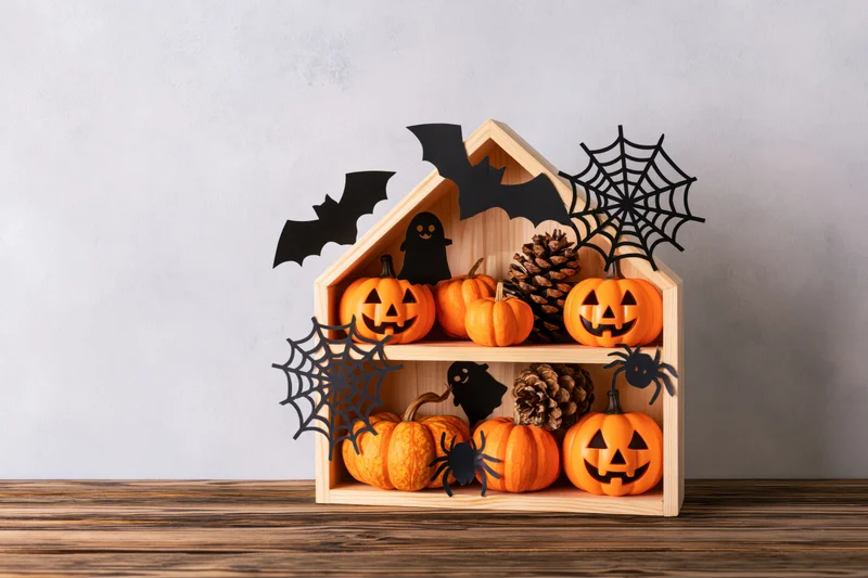 Wooden house-shaped shelf holding jack-o-lanterns and halloween decorations on a wooden surface