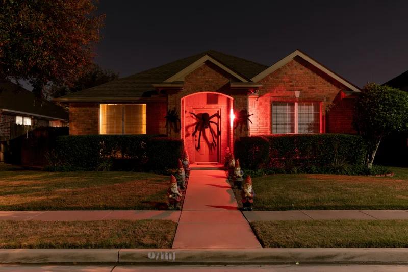 Suburban brick house decorated for halloween at night with red lighting and garden gnomes along the pathway