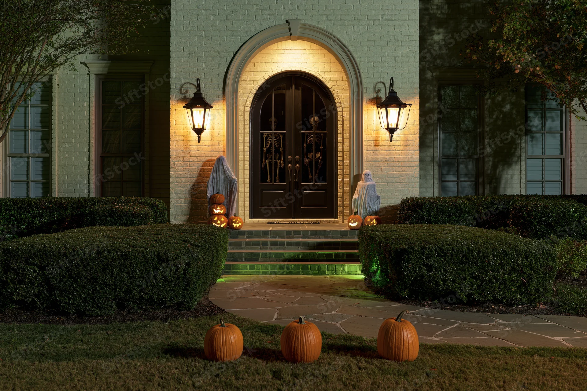 Suburban brick house front entry decorated for halloween at night with pumpkins and skeletons on porch