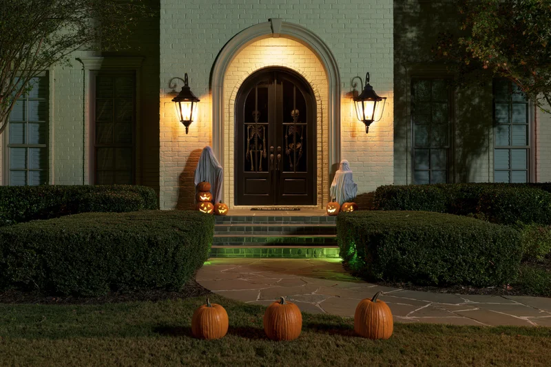 Suburban brick house front entry decorated for halloween at night with pumpkins and skeletons on porch