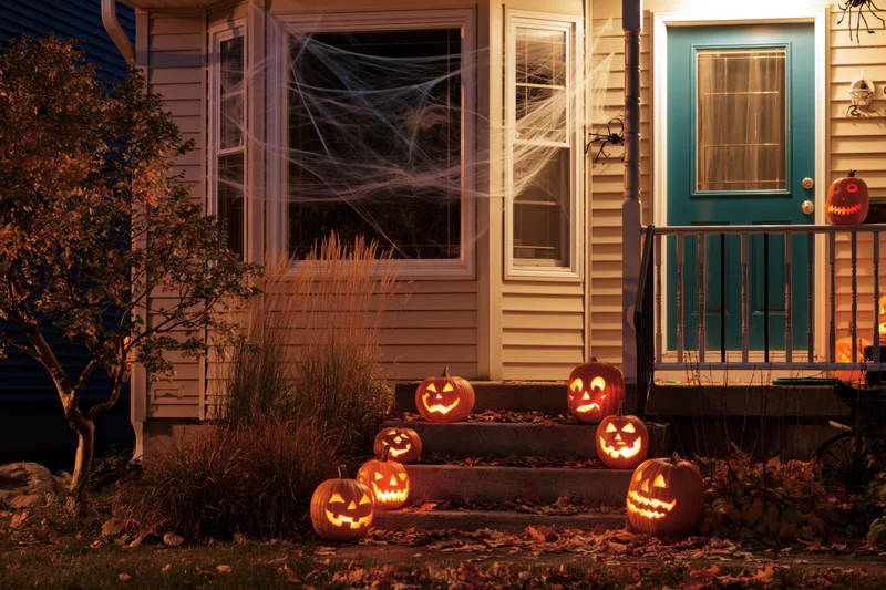 Halloween-decorated suburban house front porch with glowing jack-o-lanterns on steps at night
