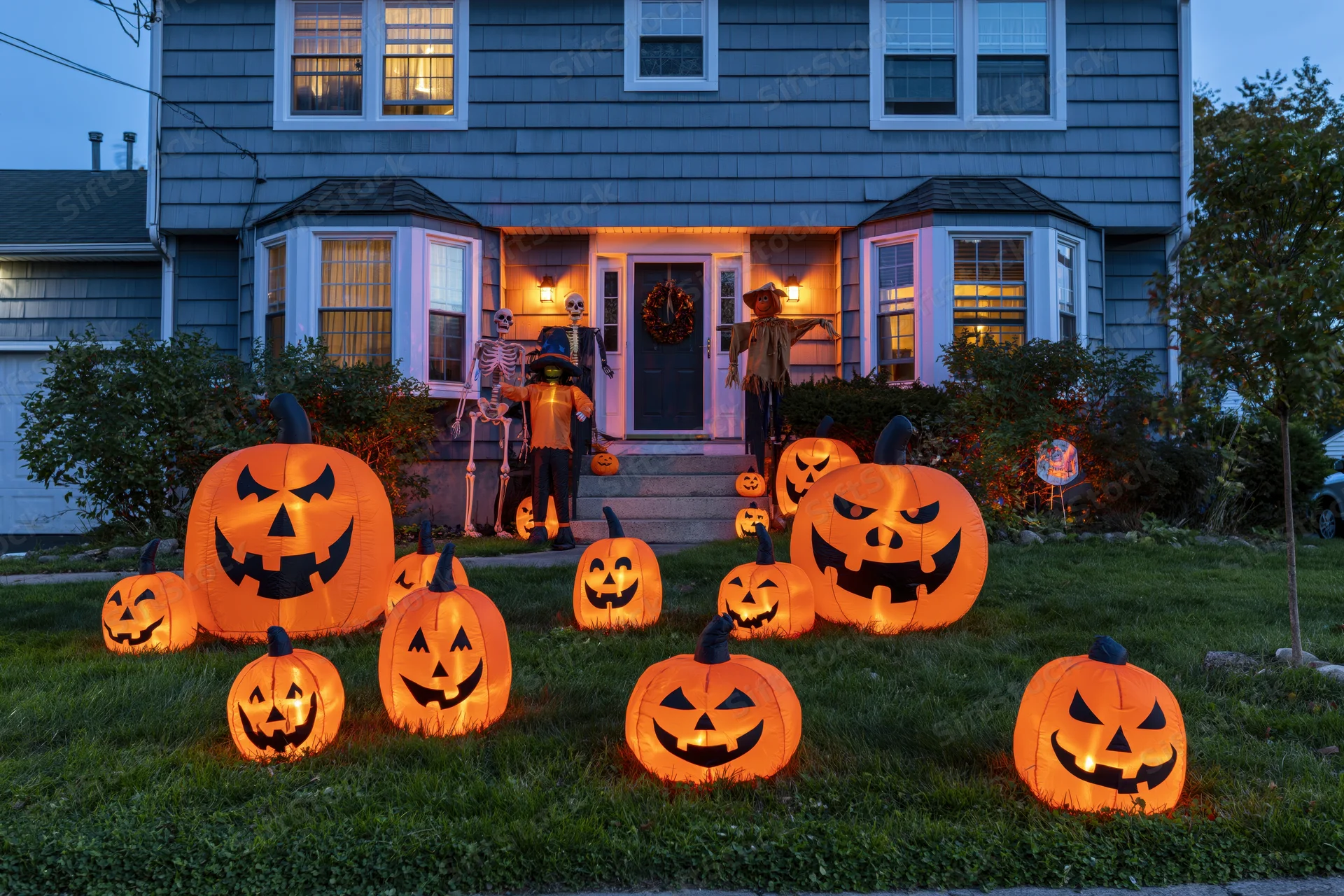 Illuminated pumpkins and halloween decorations in front yard of suburban house at dusk