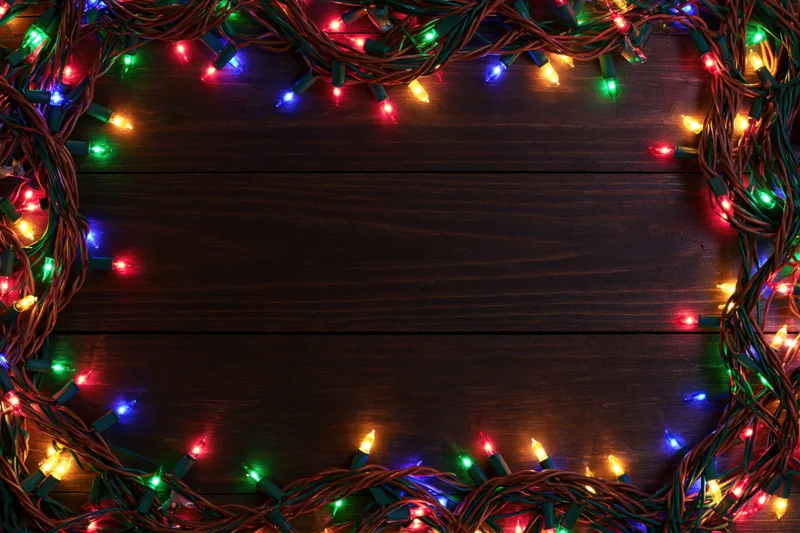 Tangled multicolored christmas string lights arranged as a frame on dark wooden surface with copyspace