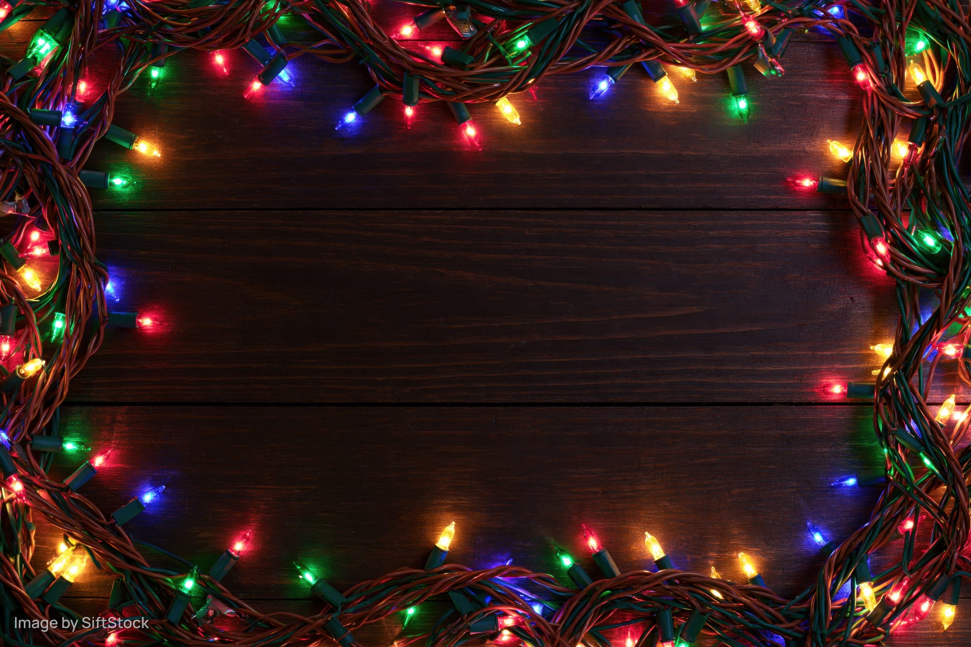 Tangled multicolored christmas string lights arranged as a frame on dark wooden surface with copyspace