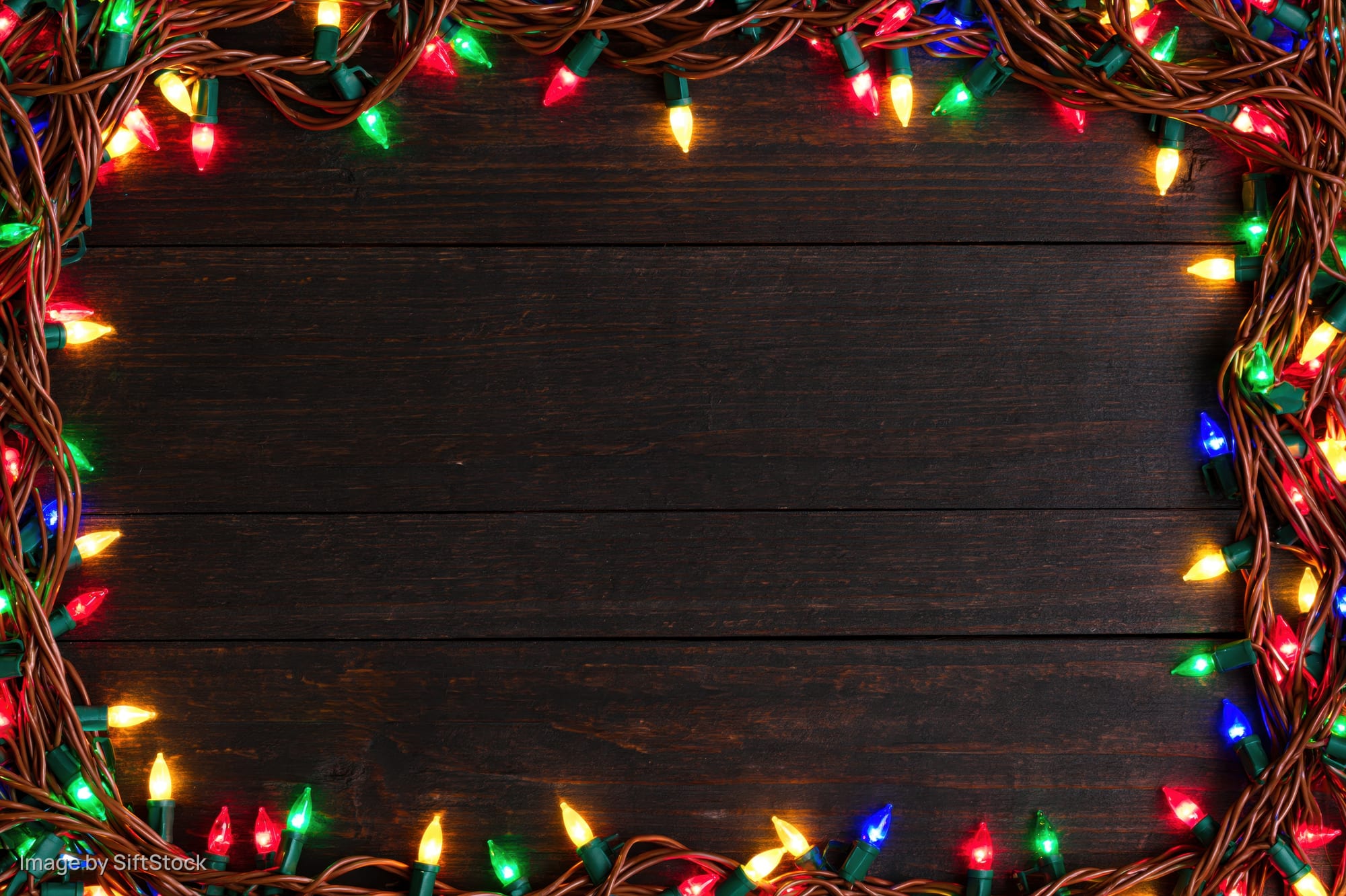 Multicolored christmas string lights arranged in a frame on dark wooden planks with copyspace in center
