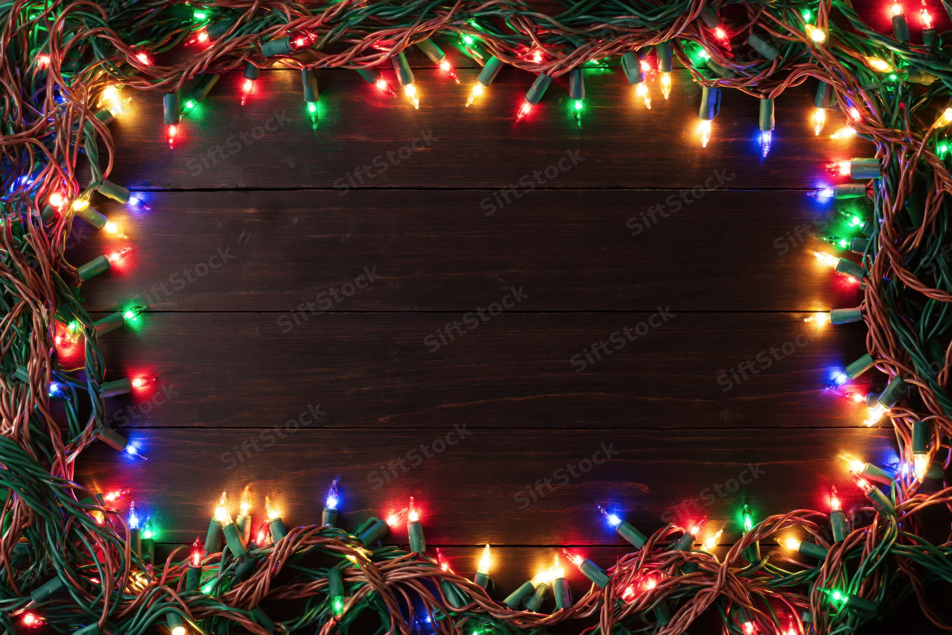 Tangled multicolored christmas string lights forming a frame on dark wooden surface with central copyspace