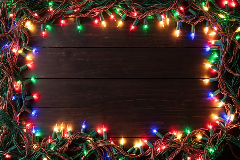 Tangled multicolored christmas string lights forming a frame on dark wooden surface with central copyspace