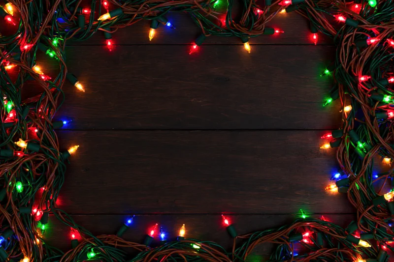 Tangled multicolored christmas string lights arranged in a frame on dark wooden surface with copyspace in center