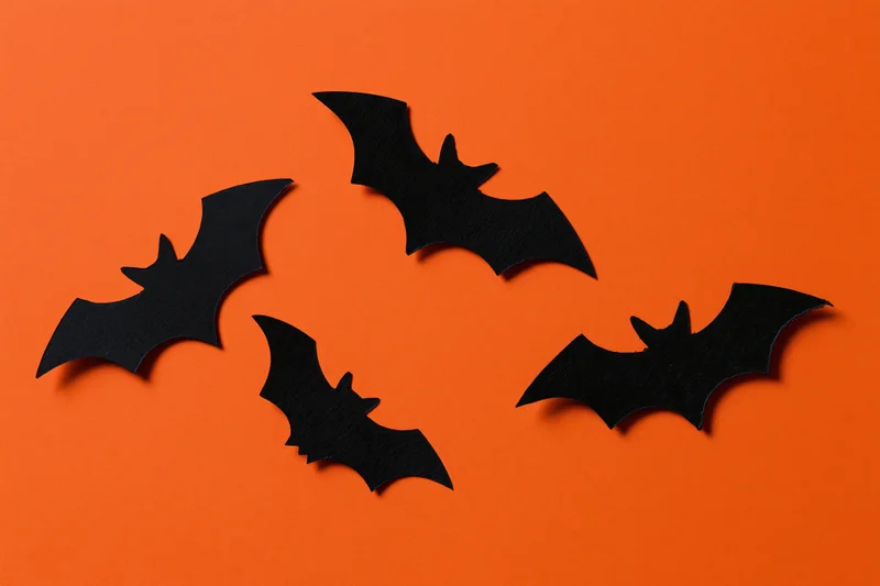 Black paper bat cutouts arranged in flight formation on orange background
