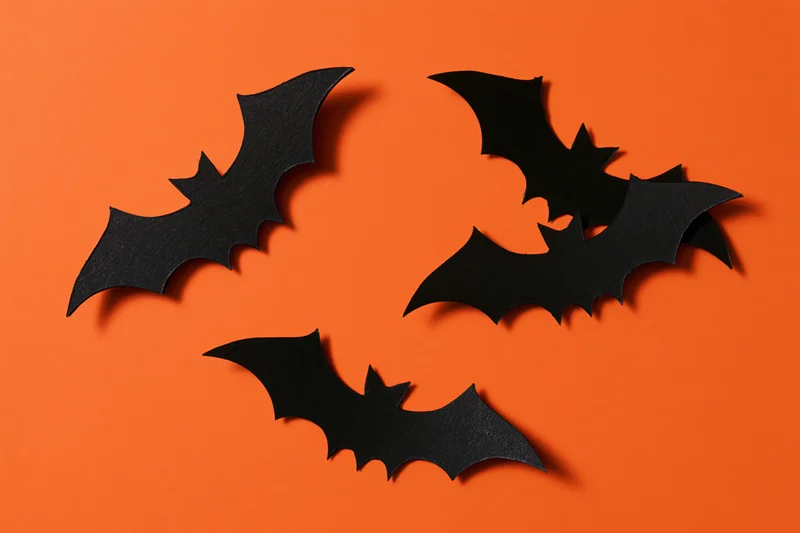 Black paper bat cutouts arranged in flight pattern on orange background