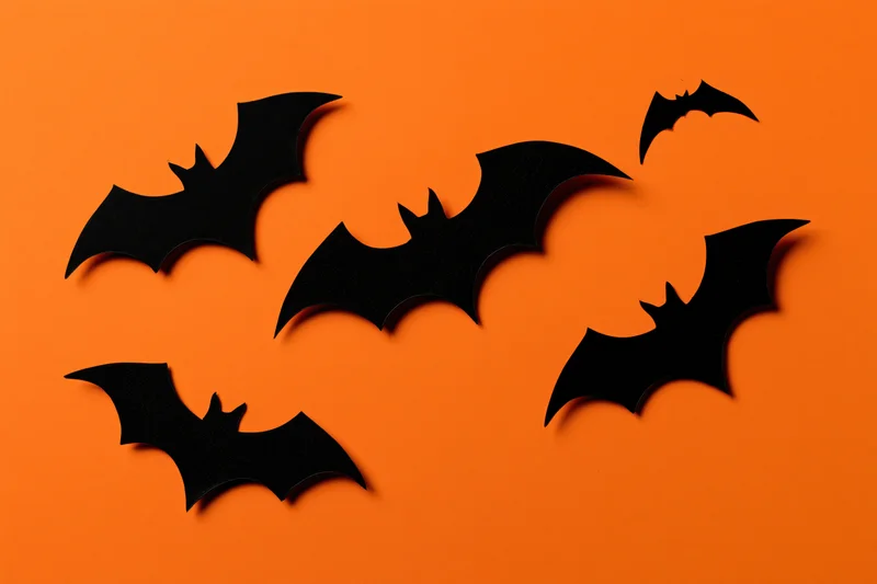 Black paper bat cutouts arranged in a loose flying pattern on orange background