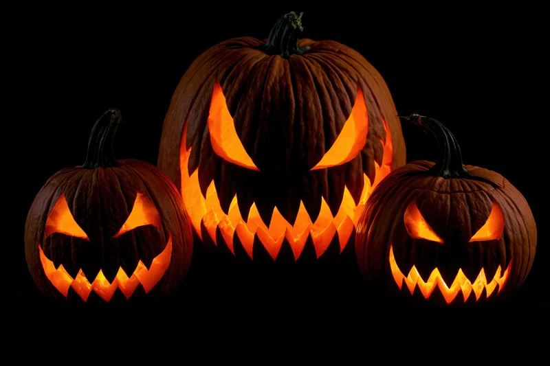 Three carved jack-o-lanterns glowing with orange light against a black background