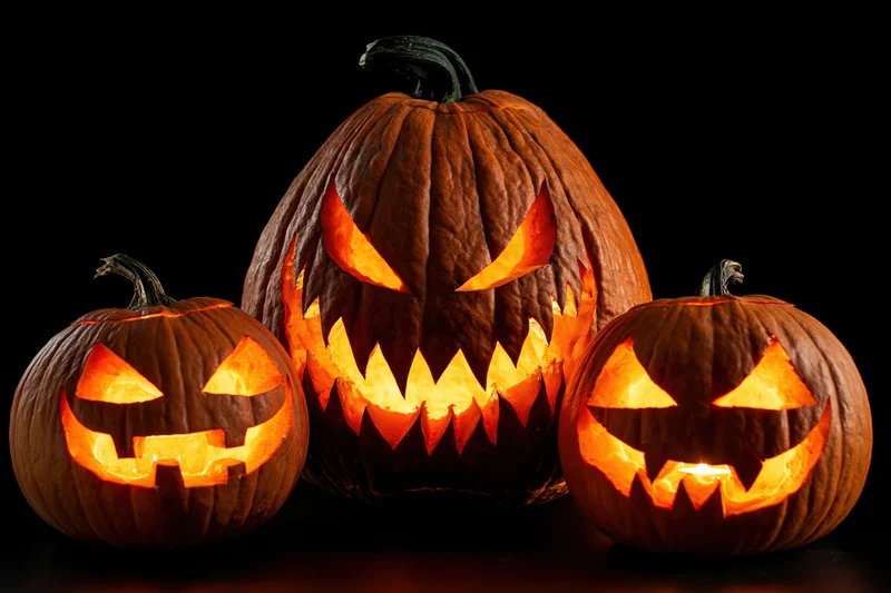 Three carved pumpkins glowing with light arranged in a tight group against a dark background