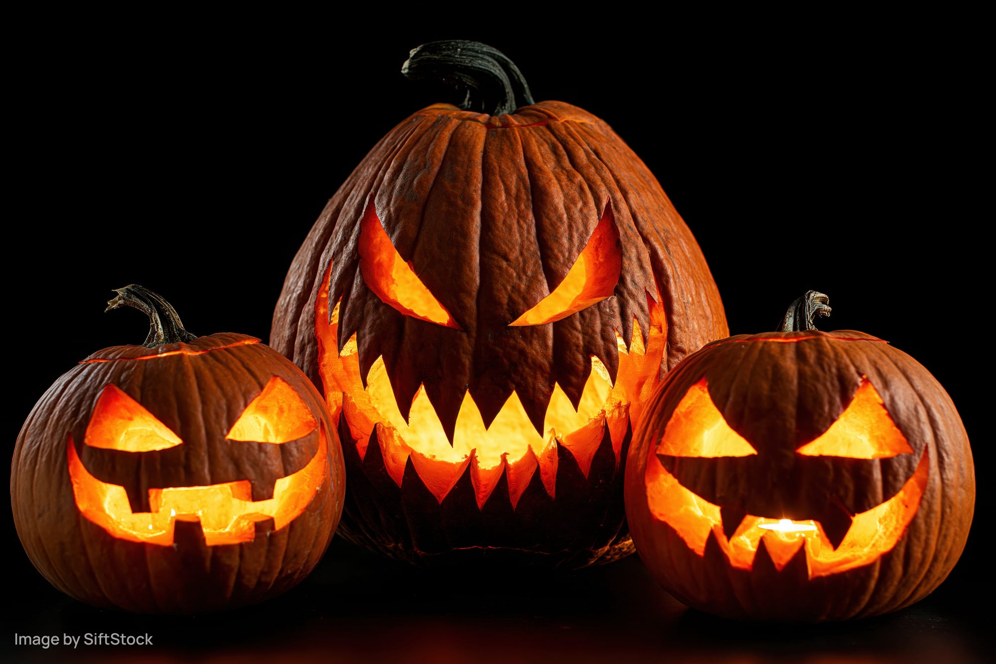 Three carved pumpkins glowing with light arranged in a tight group against a dark background